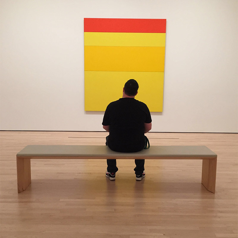A person seated in front of a simple painting of red white yellow stripes